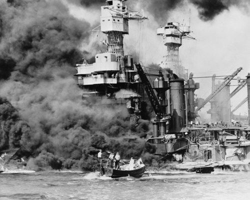 A small boat rescues a seaman from the smoking USS West Virginia.